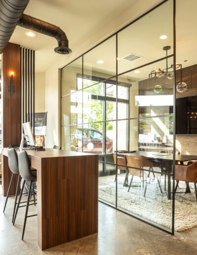 Modern office space with a communal table, glass partition, and cozy seating area.
