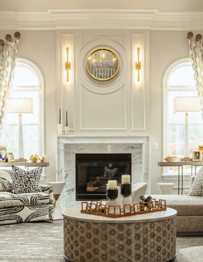 Elegant living room with neutral tones, featuring a fireplace, round wall mirror, and sophisticated furnishings.